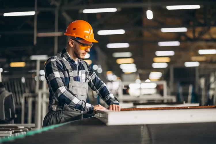 Homem usando capacete de segurança e óculos de proteção trabalhando em ambiente industrial, abordando como evitar as falhas em um compressor de ar comprimido.